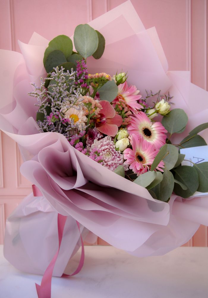 A beautiful bouquet featuring pink flowers and eucalyptus leaves wrapped in soft pink paper.