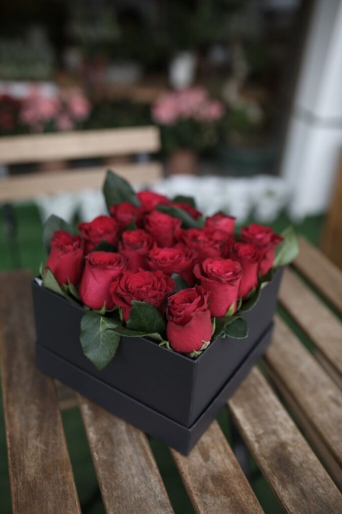 Charming box of red roses with vibrant green leaves in a stylish black container.